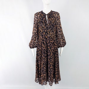 May include: A long-sleeved midi dress with a black and brown abstract print. The dress has a gathered neckline with a tie detail and a button closure. The sleeves are gathered at the shoulders and the skirt is flowy.