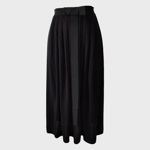 May include: A long, black skirt with a high waist and a bow detail at the front. The skirt has a flowing, pleated design and a subtle vertical stripe pattern. The fabric appears to be lightweight and suitable for various occasions.
