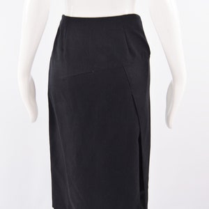 Puede incluir: Una falda negra con una abertura lateral. La falda es de largo hasta la rodilla y tiene un dise&ntilde;o simple y entallado.