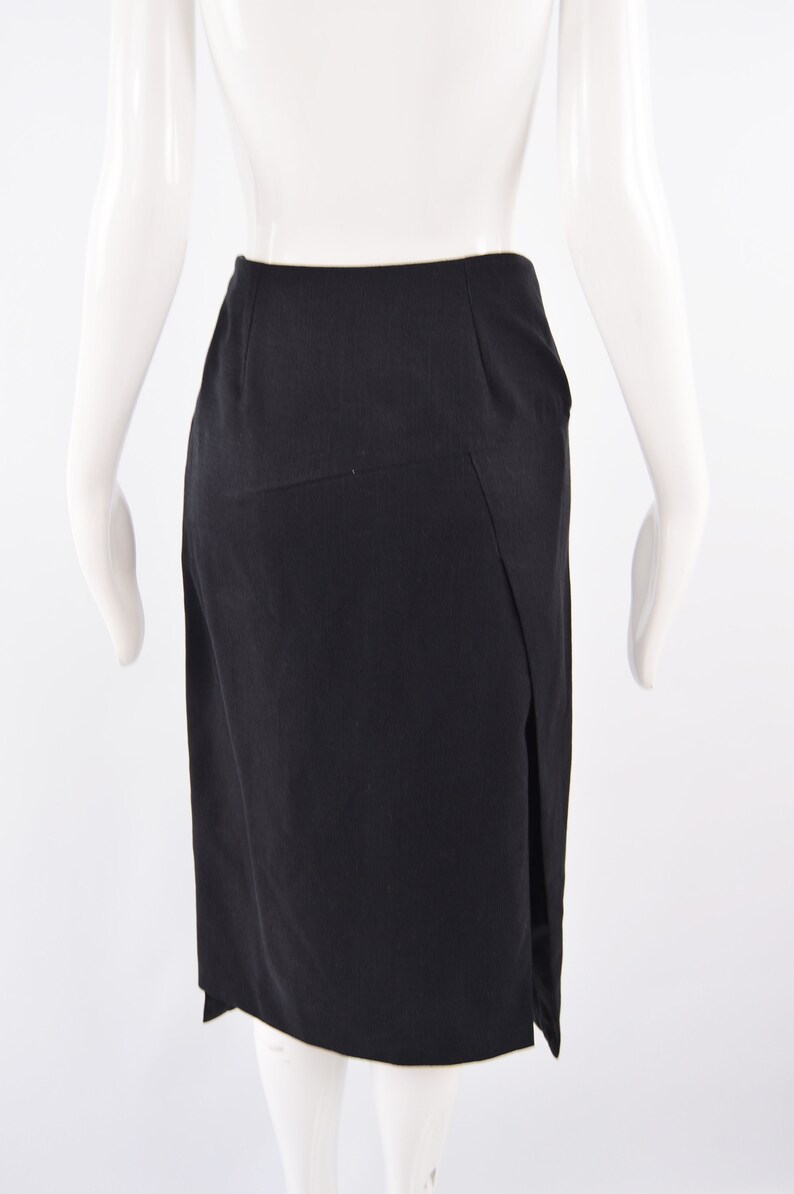 Puede incluir: Una falda negra con una abertura lateral. La falda es de largo hasta la rodilla y tiene un dise&ntilde;o simple y entallado.