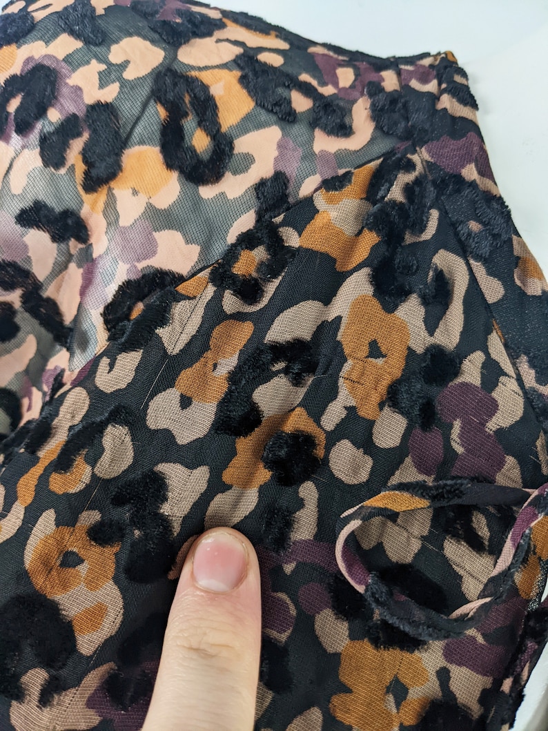 May include: Close-up of a black fabric with a brown and orange leopard print. The fabric has a velvety texture.