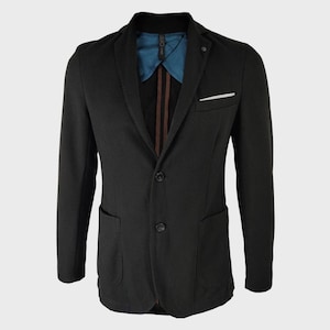 Può includere: Un blazer nero con chiusura frontale a due bottoni, risvolto dentellato e taschino sul petto con fazzoletto bianco. La fodera interna è blu ottanio con strisce verticali marroni visibili lungo l'abbottonatura centrale e il colletto.
