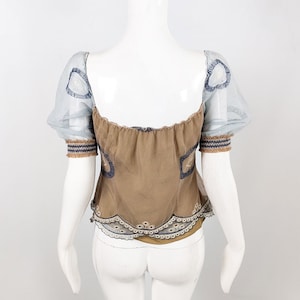May include: A brown, off-the-shoulder top with a lace trim and sheer, blue, puffed sleeves. The top has a gathered neckline and is decorated with embroidered details.