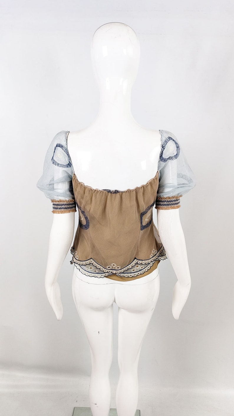 May include: A brown, off-the-shoulder top with a lace trim and sheer, blue, puffed sleeves. The top has a gathered neckline and is decorated with embroidered details.