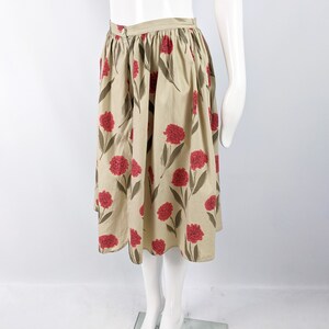 May include: A beige midi skirt with a floral print featuring red carnations. The skirt has a gathered waist and a full, A-line silhouette.