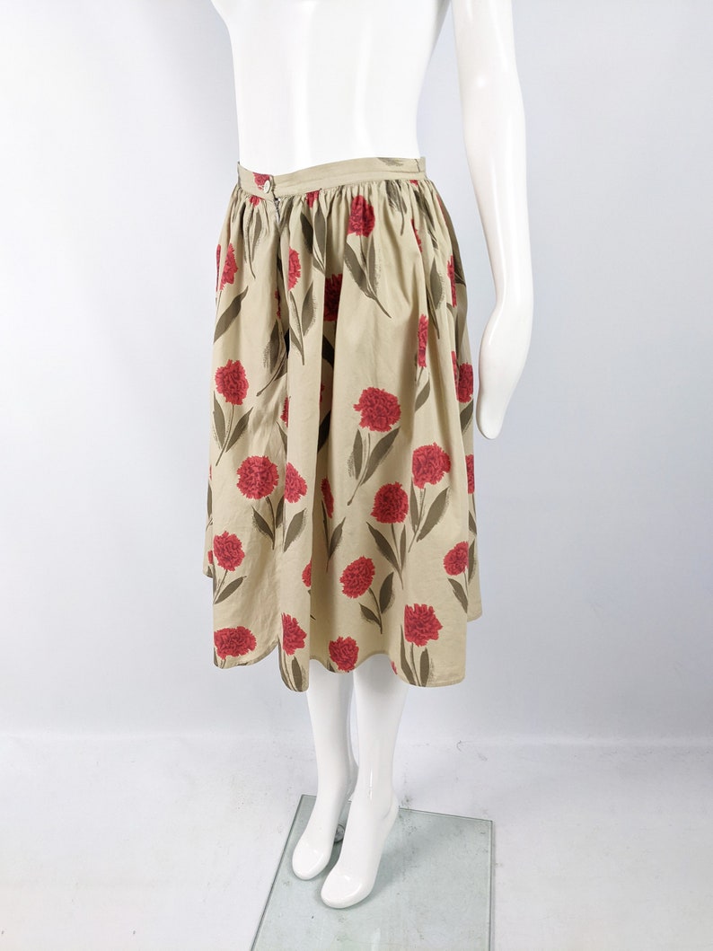 May include: A beige midi skirt with a floral print featuring red carnations. The skirt has a gathered waist and a full, A-line silhouette.