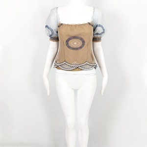 May include: A brown and white embroidered top with a lace trim. The top has short, puffed sleeves with a sheer fabric overlay.