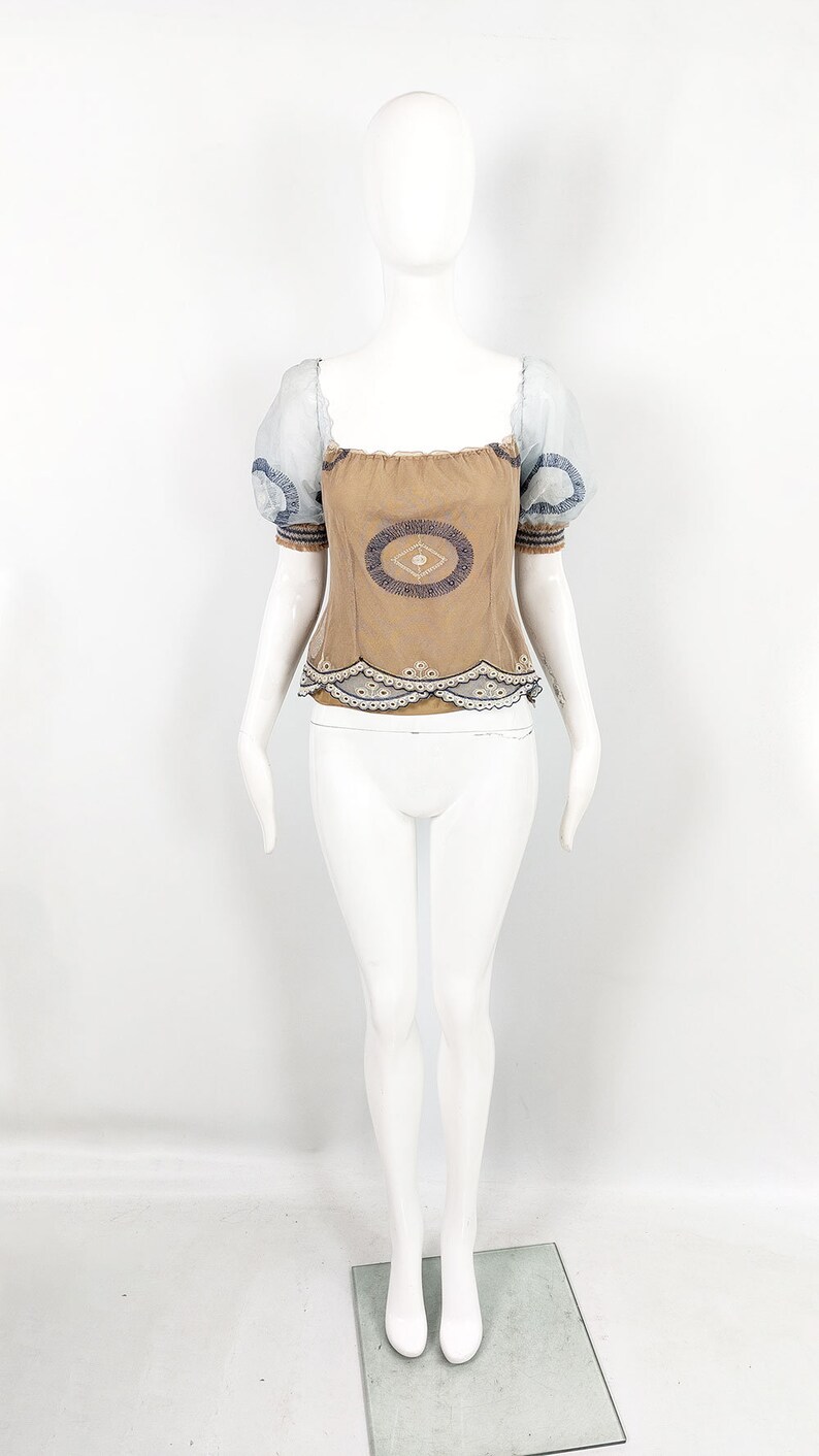 May include: A brown and white embroidered top with a lace trim. The top has short, puffed sleeves with a sheer fabric overlay.