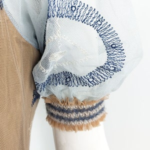 May include: A light blue and brown sheer dress with a blue embroidered design on the sleeve. The sleeve has a brown and blue striped trim.