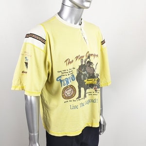 May include: Yellow short-sleeved t-shirt with a graphic print of a pirate ship and the text "The New Conquer" and "Turyo". The text "Live The Legend!" is printed below the graphic.