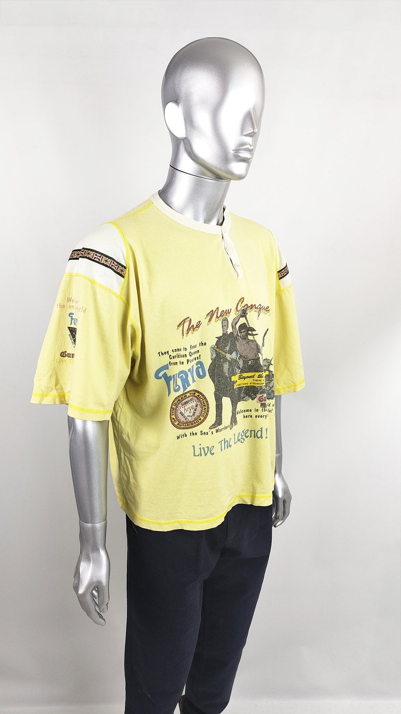 May include: Yellow short-sleeved t-shirt with a graphic print of a pirate ship and the text "The New Conquer" and "Turyo". The text "Live The Legend!" is printed below the graphic.