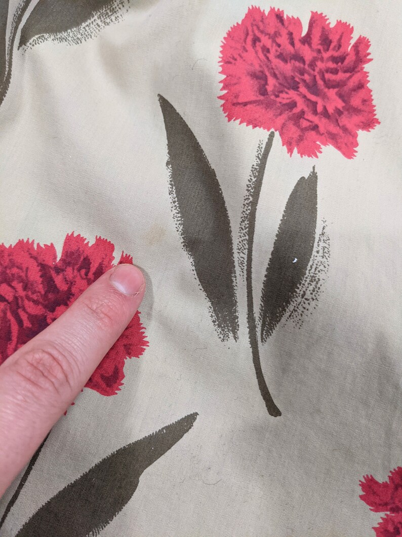 May include: Beige fabric with a repeating pattern of red carnations and dark green leaves.