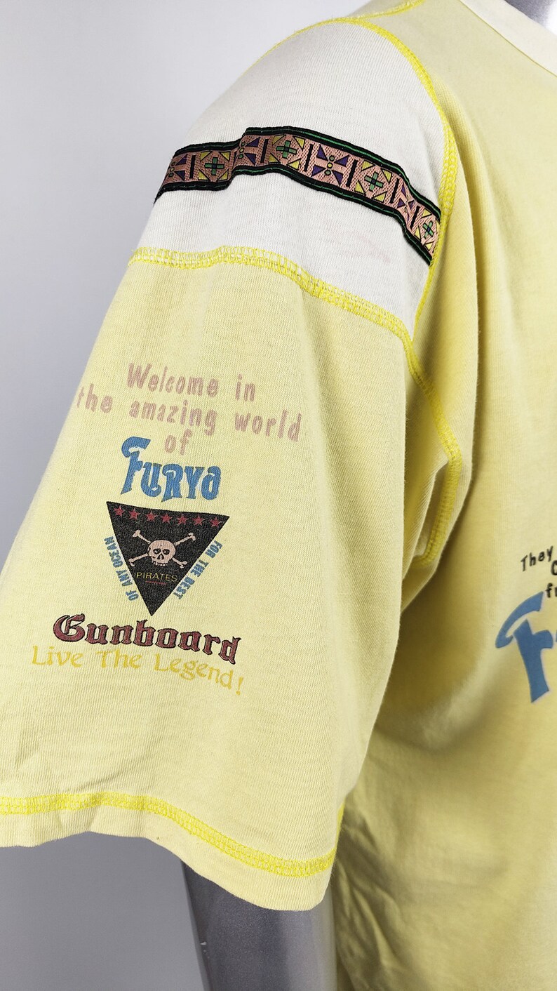 May include: Yellow short-sleeved t-shirt with a graphic print of a skull and crossbones with the text "Welcome in the amazing world of Furyo" and "Gunboard Live The Legend!"