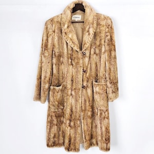 May include: A vintage Iceberg faux fur coat in shades of brown and tan. The long coat features a notched collar, two front pockets, and three brown buttons. The coat is hanging on a wooden hanger.