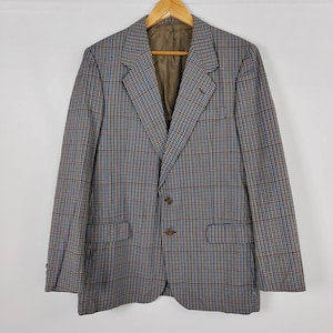May include: A vintage checked blazer in brown, blue, and tan. The jacket features a notched lapel, two front pockets, and a two-button closure. The blazer is suspended from a wooden hanger.