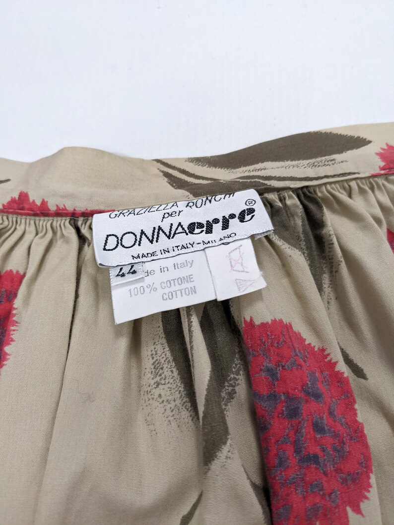 May include: A beige cotton fabric with a floral print of red and brown flowers. The fabric has a label that reads "Graziella Ronchi per Donnaerre Made in Italy - Milano 44 de in Italy 100% Cotone Cotton".