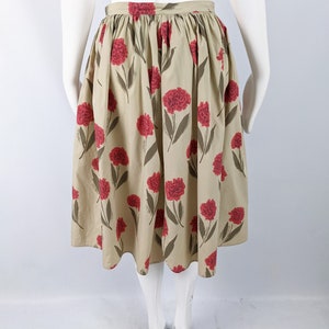 May include: A beige midi skirt with a floral print of red carnations. The skirt has a gathered waist and a full, flowing silhouette.