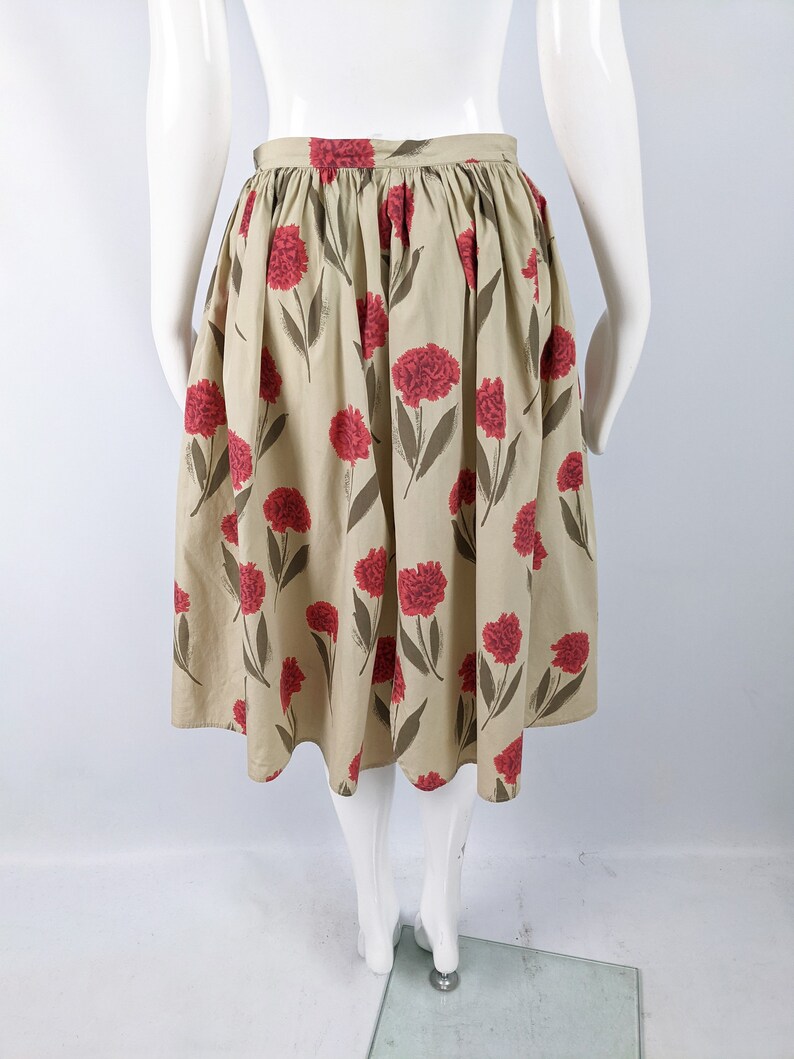 May include: A beige midi skirt with a floral print of red carnations. The skirt has a gathered waist and a full, flowing silhouette.