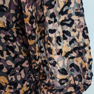 May include: A sheer black, brown, and pink leopard print blouse with long sleeves and a gathered cuff.