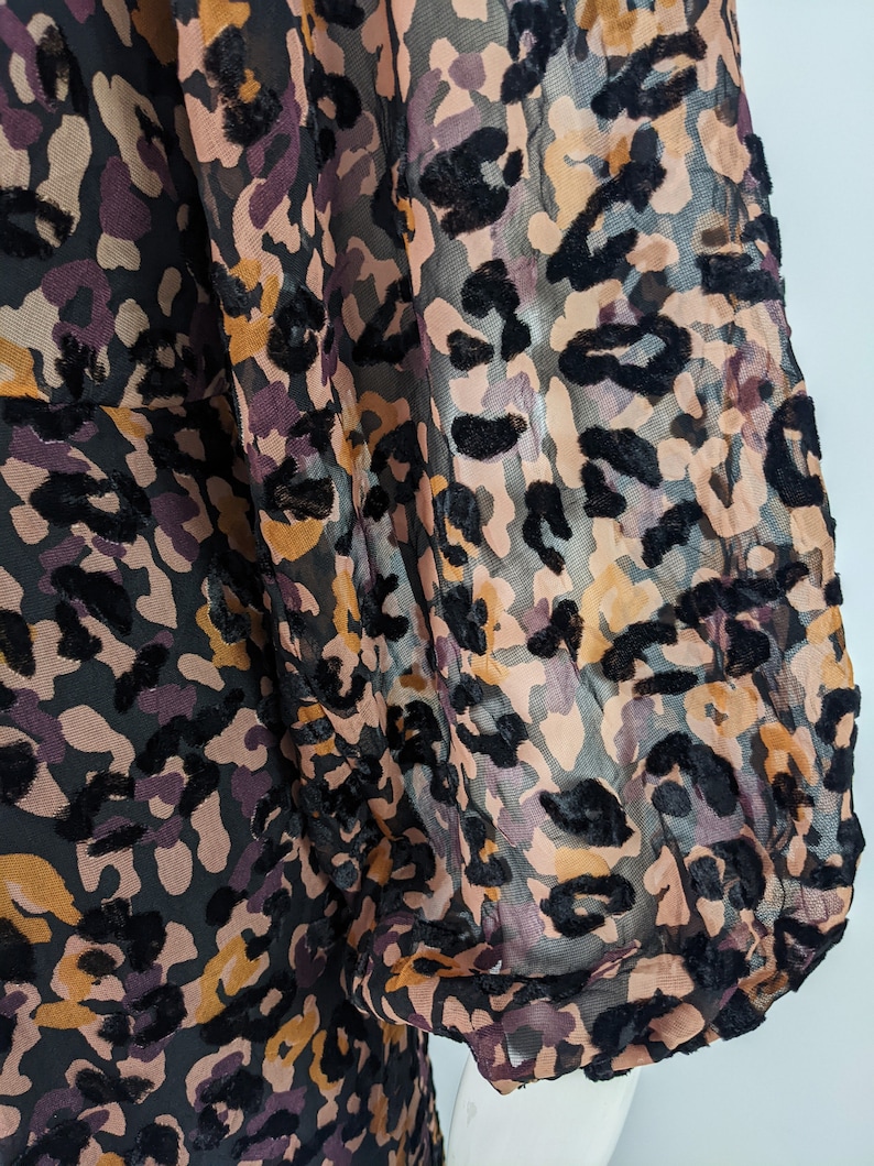 May include: A sheer black, brown, and pink leopard print blouse with long sleeves and a gathered cuff.