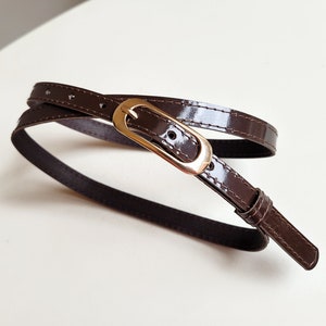 May include: A brown leather belt with a gold buckle. The belt is wrapped around itself and the buckle is visible in the centre of the image.