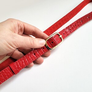 Puede incluir: Un cintur&oacute;n de cuero rojo con una hebilla dorada. El cintur&oacute;n tiene un patr&oacute;n de piel de cocodrilo.
