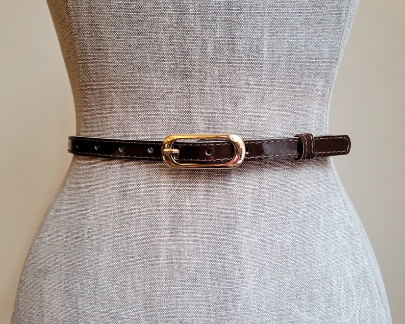 May include: A brown leather belt with a gold-toned oval buckle.