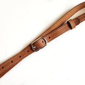 May include: A brown leather strap with a silver buckle. The strap is stitched with white thread.