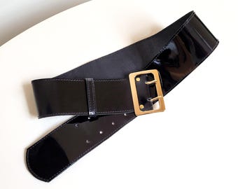 May include: A black patent leather belt with a gold buckle. The belt is wide and has a simple design.