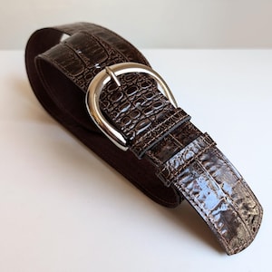 Peut inclure: Une ceinture en cuir marron avec un motif crocodile et une boucle argentée.