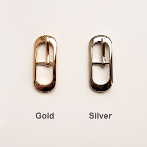 May include: Two metal belt buckles, one gold and one silver. Both buckles are oval shaped with a centre bar.