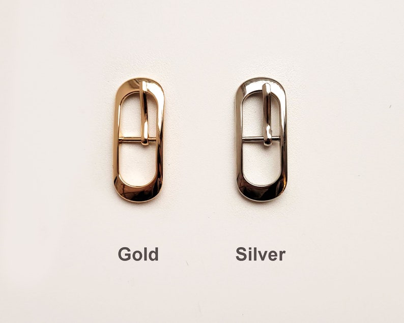 May include: Two metal belt buckles, one gold and one silver. Both buckles are oval shaped with a centre bar.