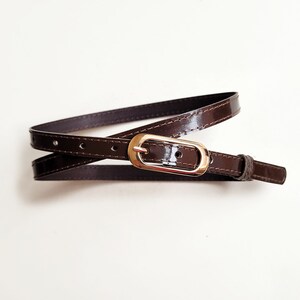 May include: A brown leather belt with a gold-toned buckle. The belt is folded in half and the buckle is visible in the centre of the image.