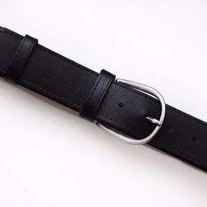 May include: A black leather belt with a silver buckle. The belt has five holes for adjusting the size.
