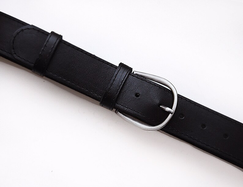 May include: A black leather belt with a silver buckle. The belt has five holes for adjusting the size.