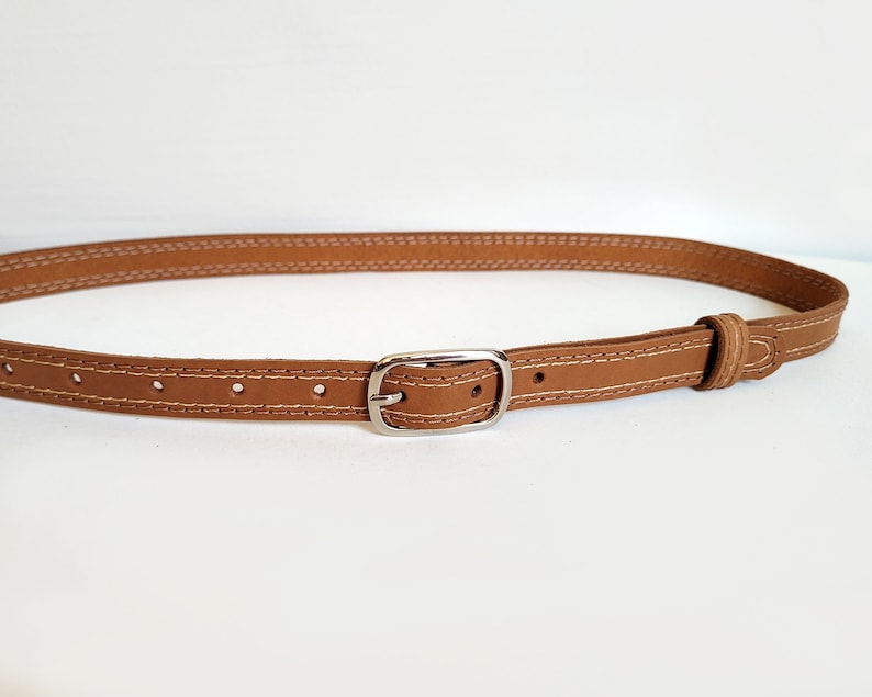 May include: A brown leather belt with a silver buckle and white stitching.