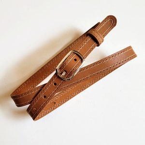 May include: A brown leather belt with a gold buckle and stitching. The belt is folded in half and the buckle is visible.