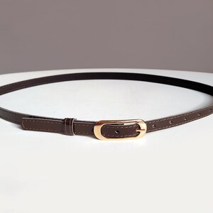 May include: A brown leather belt with a gold-toned buckle. The belt is thin and has a simple design.