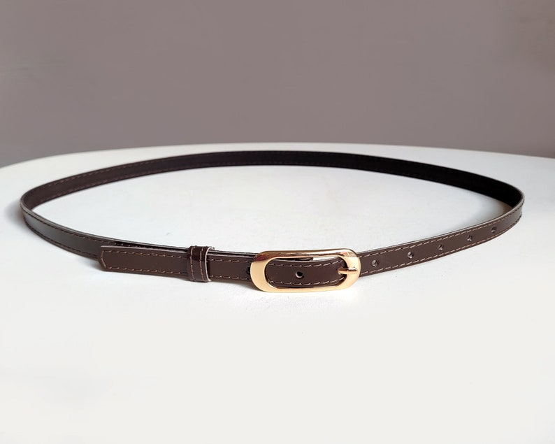 May include: A brown leather belt with a gold-toned buckle. The belt is thin and has a simple design.