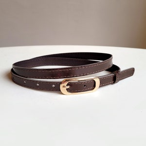 May include: A brown leather belt with a gold-toned buckle. The belt is folded in half and the buckle is visible in the centre of the image.