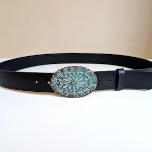 Puede incluir: Cinturón de cuero negro con hebilla ovalada turquesa con diseño floral y acabado envejecido. Un accesorio clásico para complementar diferentes atuendos.