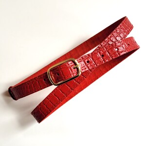 Puede incluir: Un cintur&oacute;n de cuero rojo con una hebilla dorada. El cintur&oacute;n est&aacute; hecho de cuero con estampado de cocodrilo.