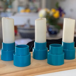 May include: Four white candles in teal blue candle holders. The candle holders are stacked in two tiers.
