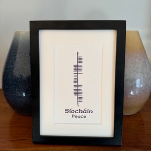 May include: A framed print with a black frame and a white mat. The print features a black and white stylized image of a fern with the text "Siochain Peace" in purple below the image.