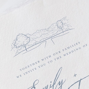 May include: A light blue wedding invitation with a landscape illustration and elegant script. The invitation reads "Together with our families, we invite you to the wedding of Emily + Trevor."