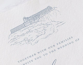 Puede incluir: Una invitación de boda con una ilustración azul de un edificio en un acantilado con vistas al océano. El texto dice "Juntos con nuestras familias, les invitamos a la boda de Emily + Trevor".