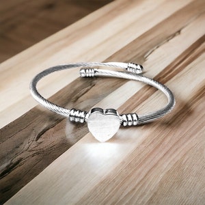 May include: A silver bangle bracelet with a heart-shaped charm. The bracelet is made of twisted wire and has a simple design.