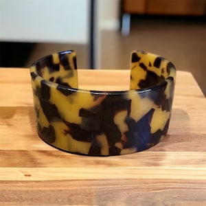 May include: A wide, yellow and brown tortoiseshell patterned bangle bracelet.