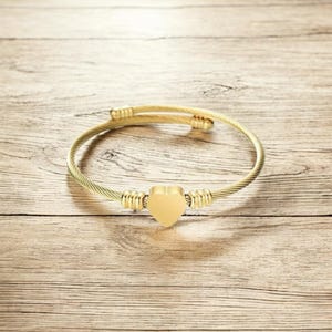 May include: A gold-toned cable bracelet with a heart-shaped charm. The bracelet is made of twisted metal and has a simple design.