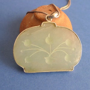 May include: A green jade pendant necklace with a floral design. The pendant is oval shaped and has a silver bail.